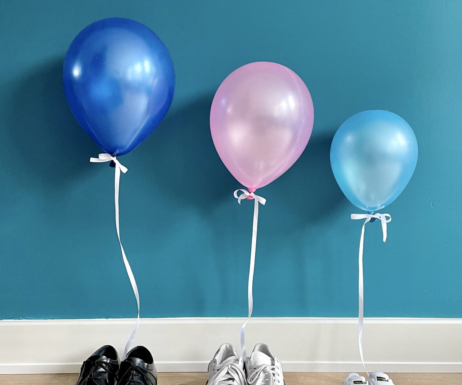 due paia di scarpe di adulto e un paio di scarpe da bebè con attaccati dei palloncini