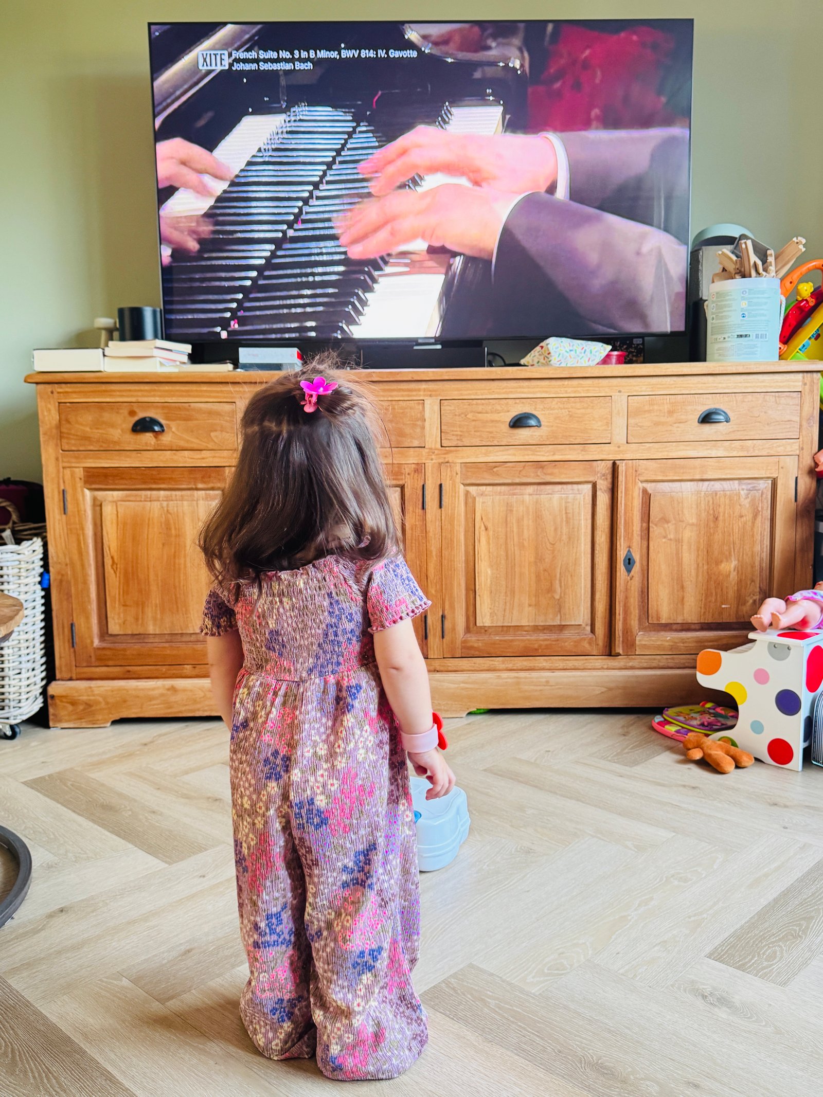 weejarig meisje dat naar een concert op tv bij het raam kijkt op een regenachtige ochtend.